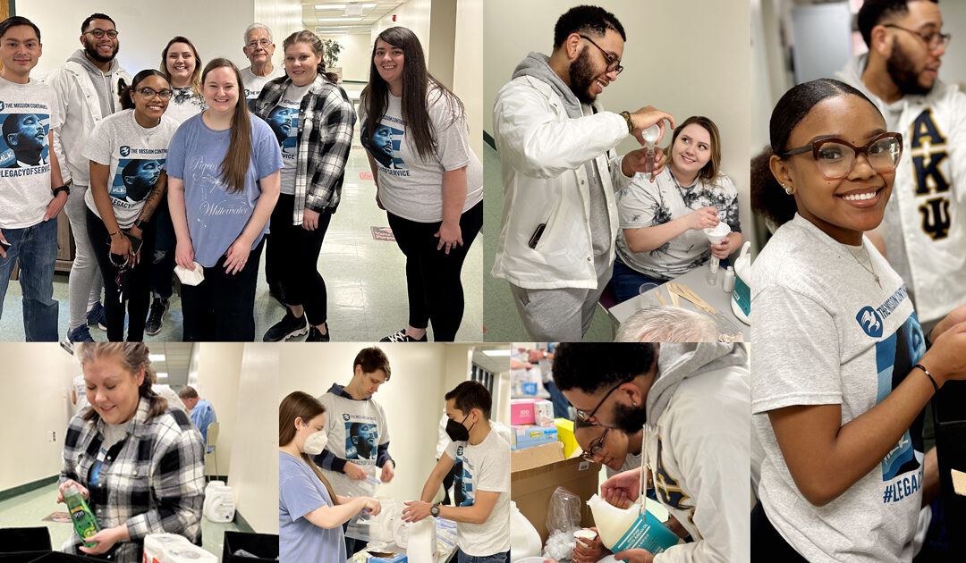 A collage of six photos showing a diverse group of people engaged in a community service activity indoors. In the top left image, eight people stand together smiling, some wearing matching t-shirts with a graphic and text. The top middle image shows a man pouring a liquid into a cup held by a seated woman. The top right image features a smiling woman wearing glasses and a matching t-shirt, with a man in the background. The bottom left image captures a woman in a plaid shirt holding a bottle. The bottom middle image shows three people, two wearing masks, working together with supplies on a table. The bottom right image depicts two people closely working with cups and containers. The setting appears to be a hallway or common area with a tiled floor and fluorescent lighting.