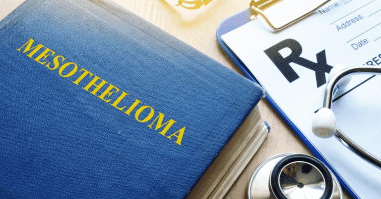 A blue book with the title "MESOTHELIOMA" in yellow letters, placed next to a medical prescription pad with "Rx" prominently displayed, and a stethoscope resting nearby on a wooden surface.