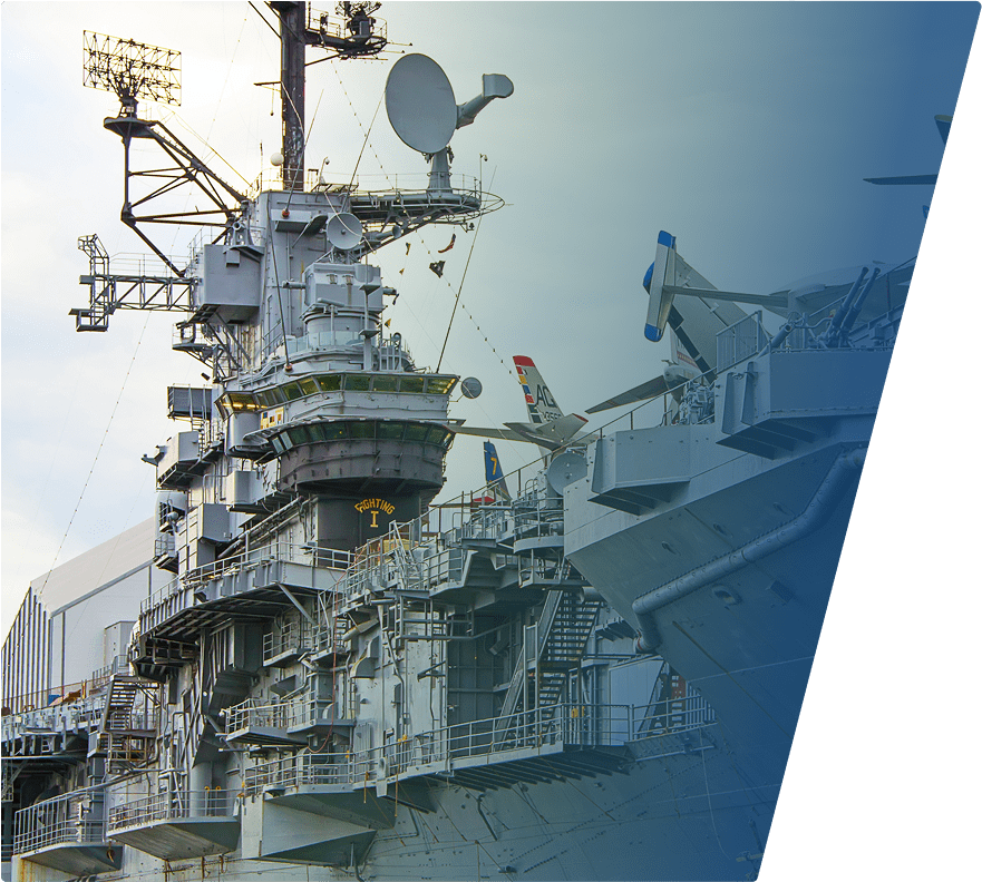 Aircraft carrier with visible radar equipment, antennas, and aircraft tails on the deck. The ship's superstructure is detailed with various platforms, railings, and communication devices. The image has a blue gradient overlay on the right side.
