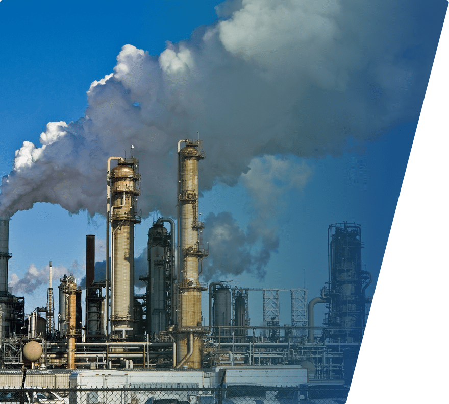 Industrial refinery with multiple tall metal towers and pipes emitting thick white smoke against a clear blue sky.