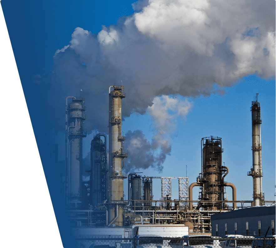 Industrial refinery towers emitting thick white smoke against a clear blue sky.
