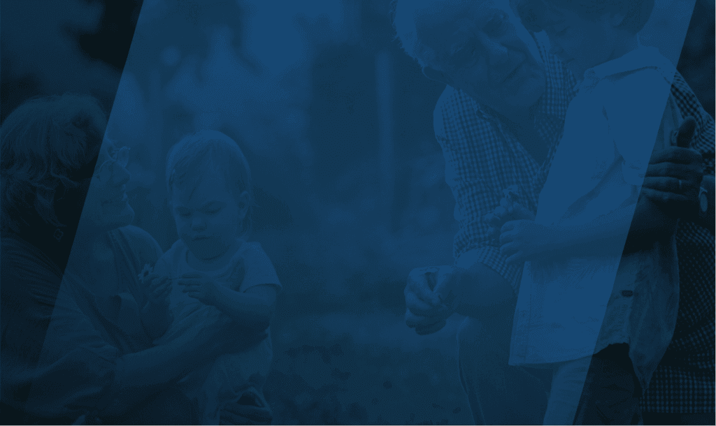 An elderly woman holding a toddler and an elderly man kneeling next to a young boy, both adults and children are holding small flowers, outdoors in a natural setting.