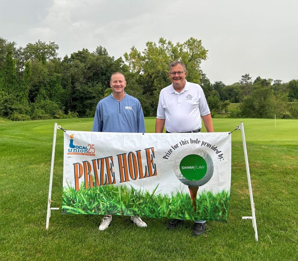 Two men standing behind a "Prize Hole" banner on a golf course. The man on the left is wearing a blue long-sleeve shirt with "IMPACT" on it and white shoes. The man on the right is wearing a white polo shirt, glasses, and dark shoes. The banner features a golf ball on a tee with the text "Prize for this hole provided by: SWMW LAW" and the Local Union 25 logo. The background shows green grass, trees, and a cloudy sky.