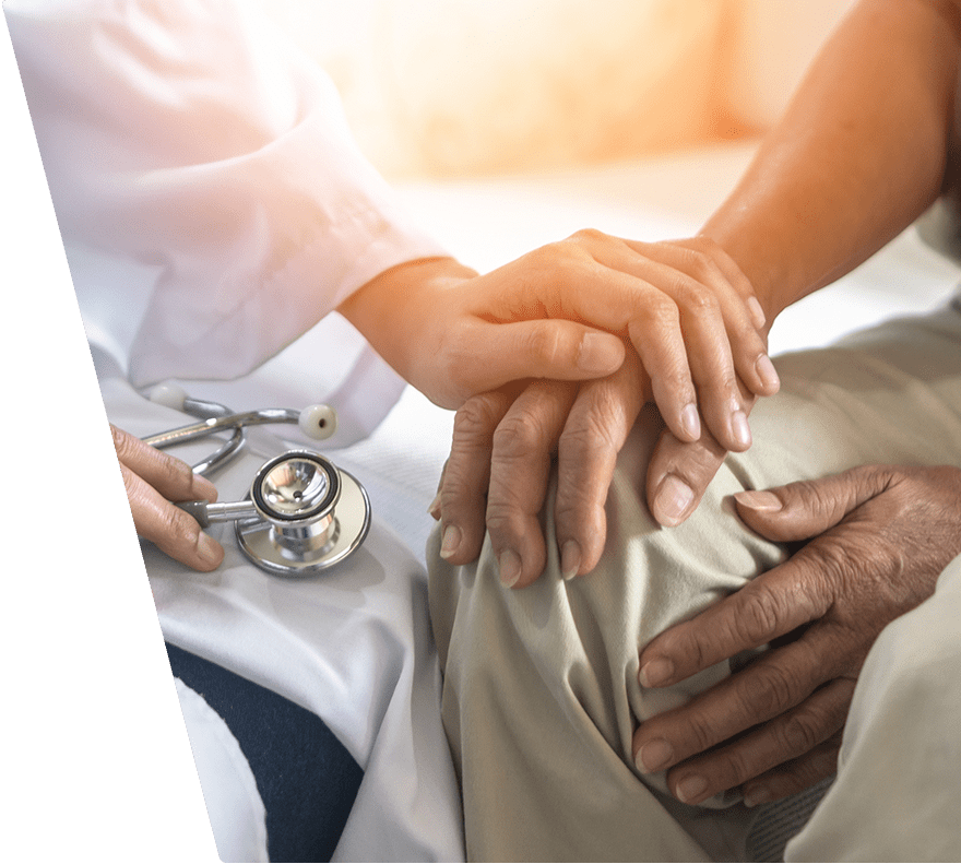 A healthcare professional in a white coat gently holds the hands of an elderly person resting on their lap. A stethoscope lies nearby, symbolizing medical care and compassion. The scene conveys support and empathy in a clinical setting.